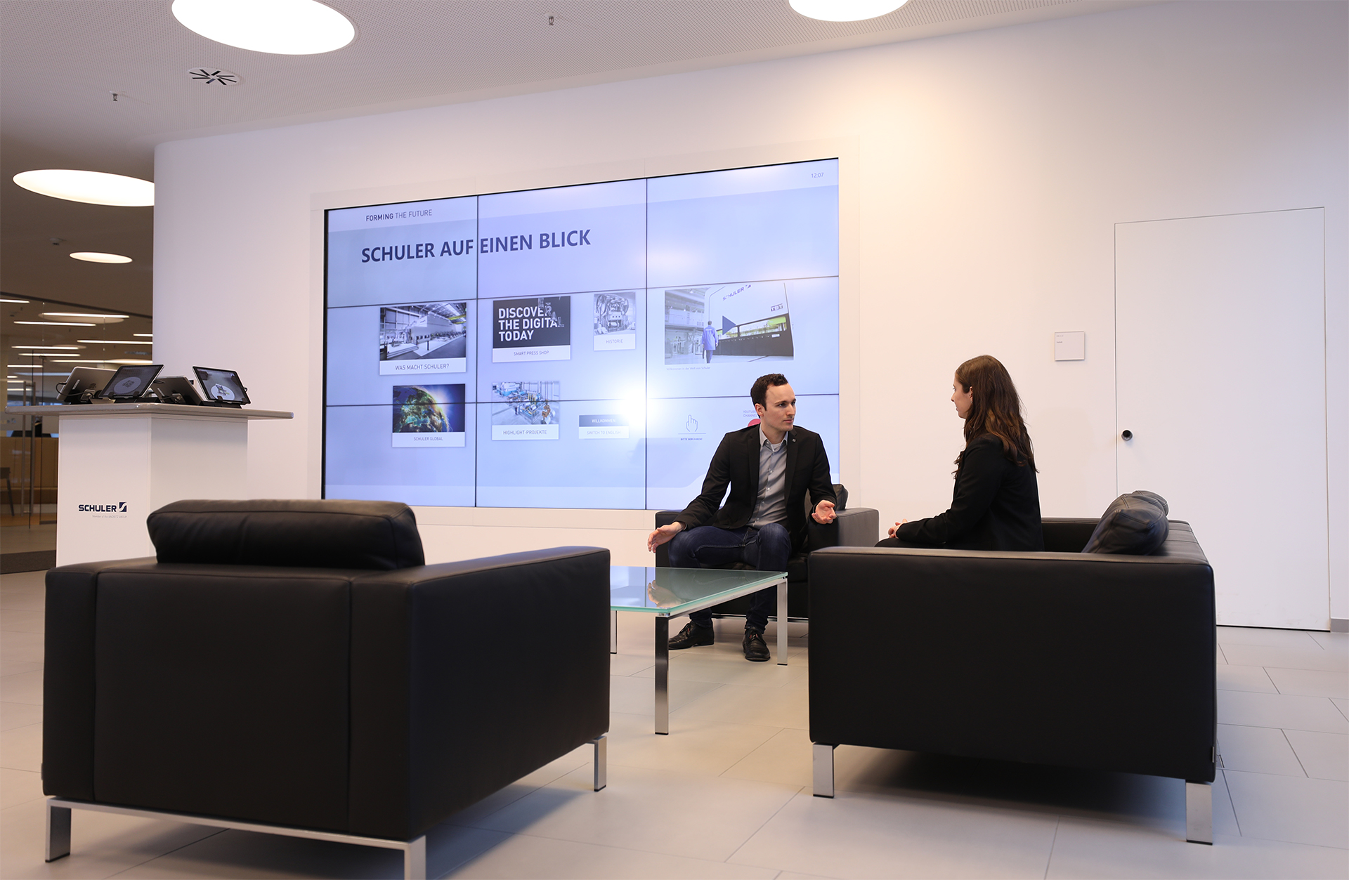 In the entrance area, a seating area invites you to spend some time with colleagues or visitors. An impressive large screen in the form of an interactive multi-touch Powerwall stages the Schuler brand and its products there. Tailor-made user interfaces powered by smartPerform inform about the company's considerable history, show examples of applications in the various market segments or provide a glimpse of highlight projects.