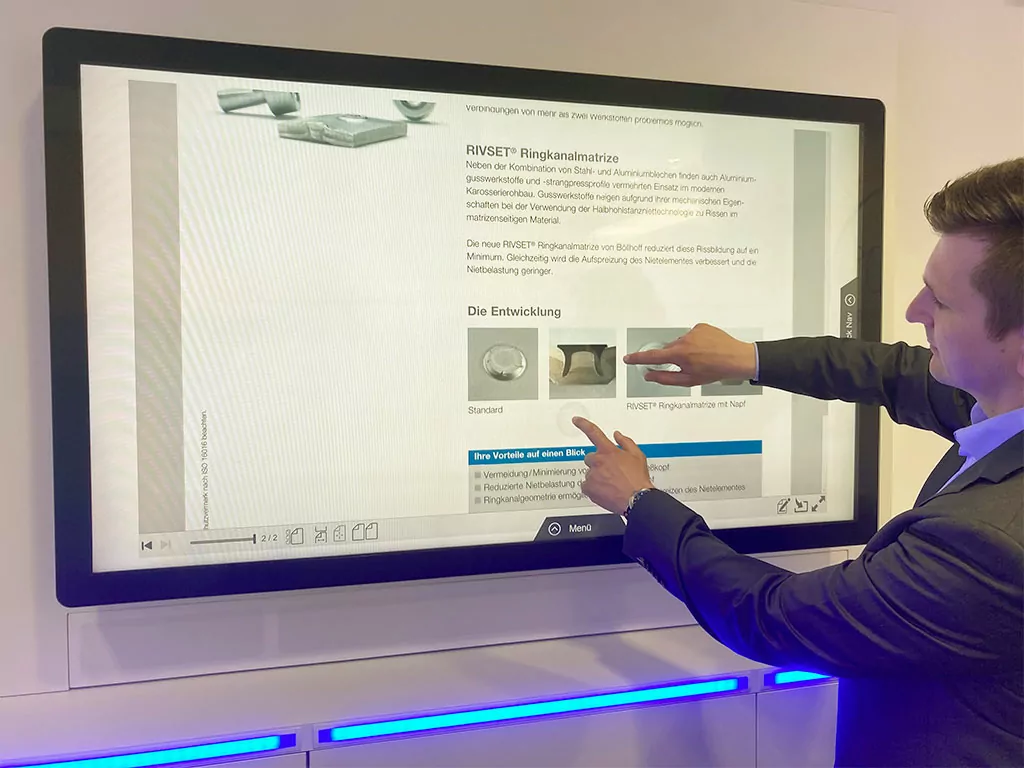 Im Eingangsbereich lädt eine Sitzecke zum Verweilen ein. Ein beeindruckender Großbildschirm in Form einer interaktiven Multi-Touch Powerwall inszeniert dort die Marke Schuler und deren Produkte.