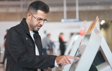 Mann bedient ein Self-Check-in-Terminal am Flughafen.