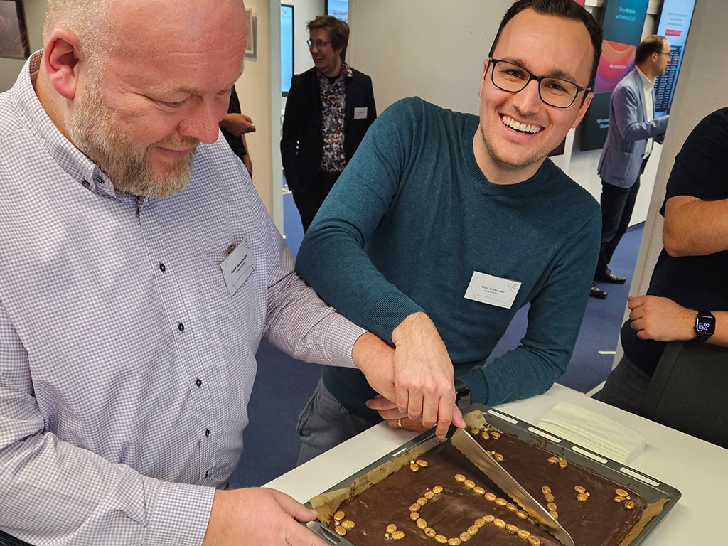 Zwei Männer schneiden einen Schokoladenkuchen an.