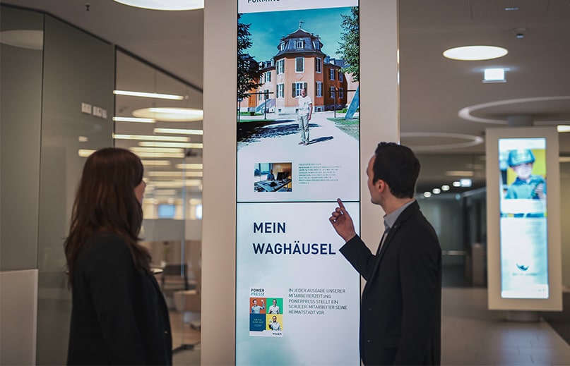 Zwei Personen betrachten digitalen Bildschirm im Büroflur